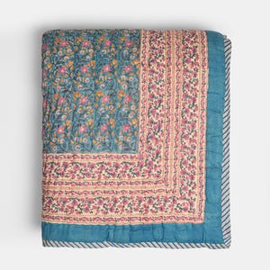 Peut inclure: Une couverture matelassée pliée avec un motif floral. La couverture présente un fond bleu sarcelle avec des fleurs roses et oranges. Une section crème avec des rayures florales roses borde la section bleu sarcelle. Les bords sont bleu sarcelle avec une bordure rayée.