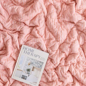 May include: A pink and white striped quilt with a book titled "HOME THERAPY" by Anita Yokota. The quilt has a textured, quilted design. The book cover features a bedroom scene.