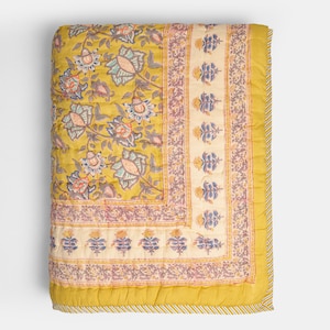 May include: A yellow floral quilt with a repeating pattern of large flowers in shades of blue, pink, and green. The quilt has a cream-colored border with a repeating floral design and a ruffled edge. The quilt measures approximately 70 x 90 inches.