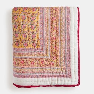 Op de afbeelding: Een gele en roze quilt met bloemenpatroon op een witte achtergrond en een rode rand. De quilt is gemaakt van katoen en met de hand gestikt.