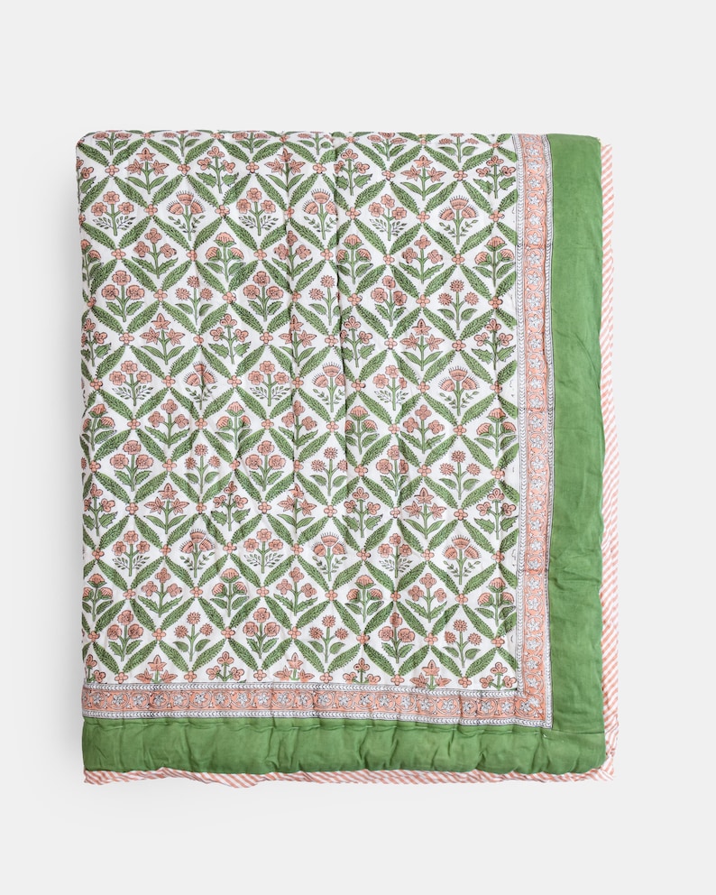 May include: A floral patterned quilt featuring a repeating design of pink flowers and green leaves on a white background. The quilt has a green border and a pink and white striped edge. The overall design is symmetrical and visually appealing.