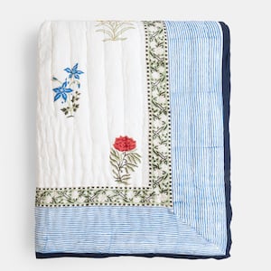 Puede incluir: Manta acolchada blanca con dise&ntilde;os florales azules y rojos y borde a rayas azules. La manta tiene un ribete azul marino. Los dise&ntilde;os florales incluyen flores azules y rojas con hojas verdes. La manta est&aacute; doblada.