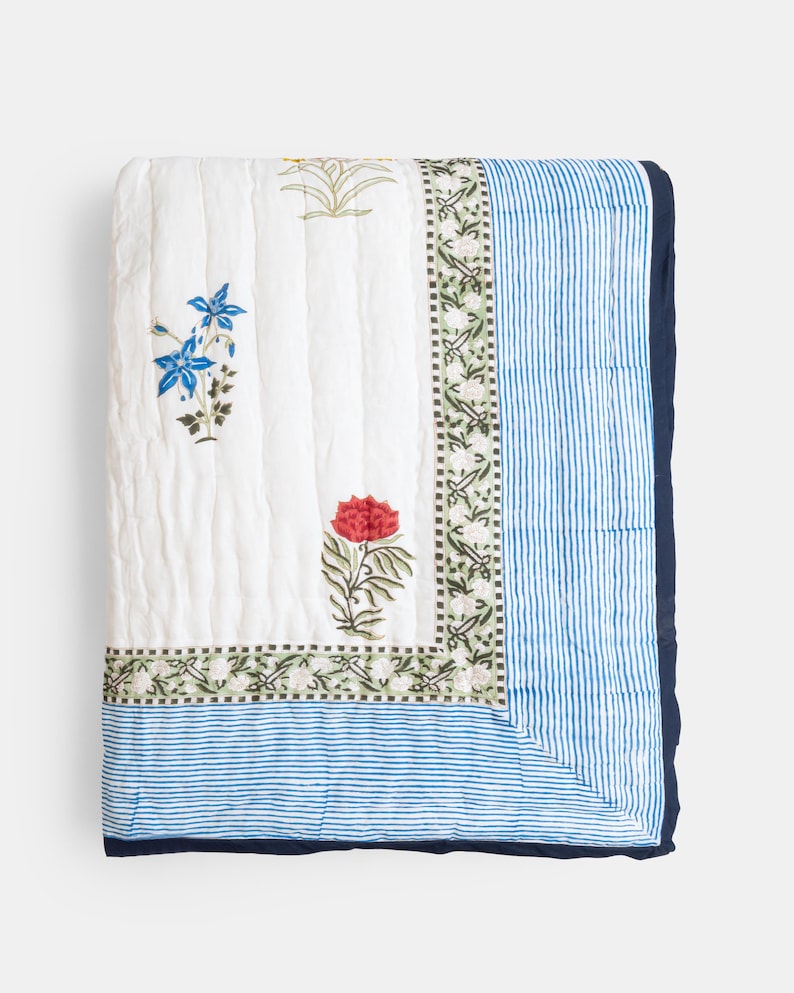 Puede incluir: Manta acolchada blanca con dise&ntilde;os florales azules y rojos y borde a rayas azules. La manta tiene un ribete azul marino. Los dise&ntilde;os florales incluyen flores azules y rojas con hojas verdes. La manta est&aacute; doblada.