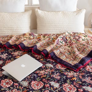 K&ouml;nnte beinhalten: Eine dunkelblaue Blumenbettw&auml;sche mit rotem Rand und einem Laptop darauf. Die Bettw&auml;sche ist aus Baumwolle und hat ein traditionelles indisches Design.