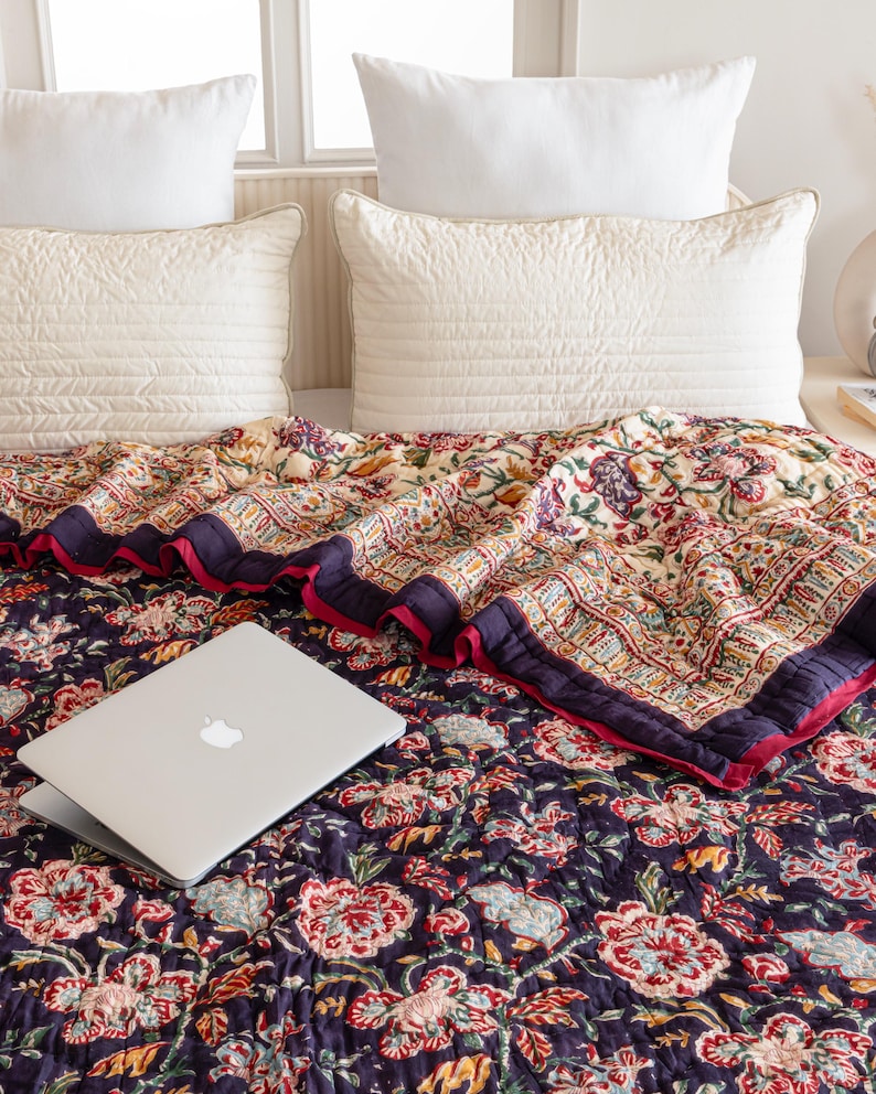K&ouml;nnte beinhalten: Eine dunkelblaue Blumenbettw&auml;sche mit rotem Rand und einem Laptop darauf. Die Bettw&auml;sche ist aus Baumwolle und hat ein traditionelles indisches Design.