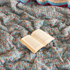 Peut inclure: Une courtepointe à motifs floraux bleus et roses avec un livre posé dessus.
