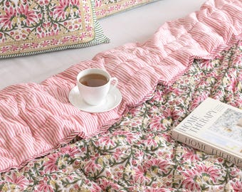 May include: A bed set featuring a floral quilt and pillow with pink, green, and white patterns, and a pink striped bed runner. A white teacup and saucer are on the runner, and a book titled "HOME THERAPY" rests on the quilt.