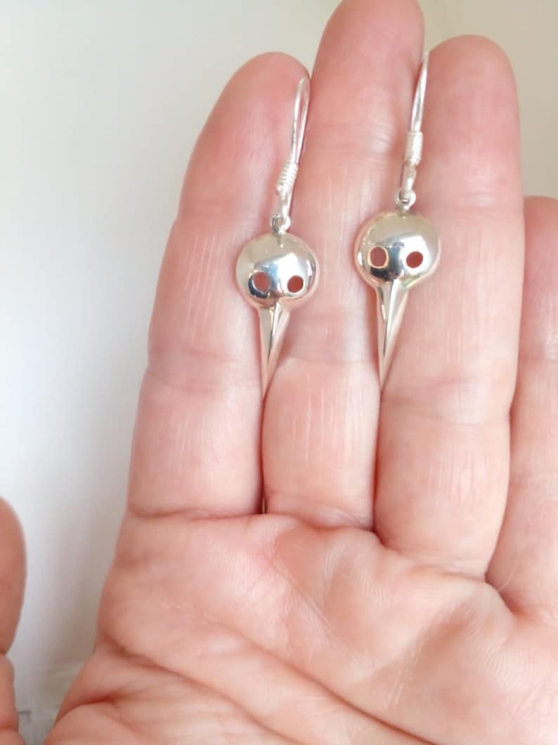 May include: A pair of silver earrings with a bird skull design. The earrings are dangle style and have a hook closure.