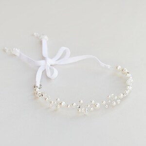 May include: A delicate hair vine featuring small white pearls and clear crystals set on a thin silver-toned wire. The piece is accented with a white ribbon tied into a bow at one end, providing a secure and adjustable fit for styling.