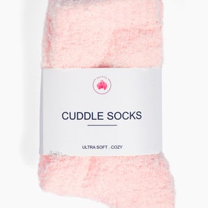 May include: Pink fuzzy socks with the text "CUDDLE SOCKS" and "ULTRA SOFT. COZY" on a white label.