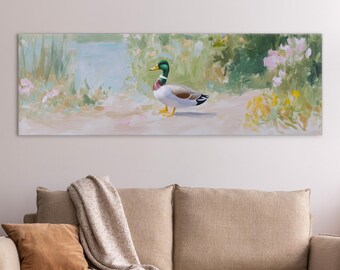 May include: A rectangular canvas print featuring a painting of a mallard duck in a natural setting. The duck has a green head, white neck ring, and brown body. The background includes a pond, greenery, and pink and yellow flowers. The artwork is displayed above a beige sofa.