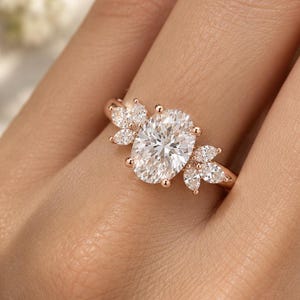 Könnte beinhalten: Ein Ring aus Roségold mit einem zentralen, oval geschliffenen weißen Edelstein, der auf jeder Seite von drei kleineren, marquise-geschliffenen weißen Edelsteinen flankiert wird, auf einer schmalen Ringschiene.