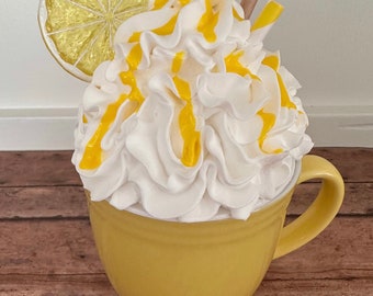 May include: A yellow ceramic mug filled with white whipped cream topped with a lemon slice and yellow sauce.