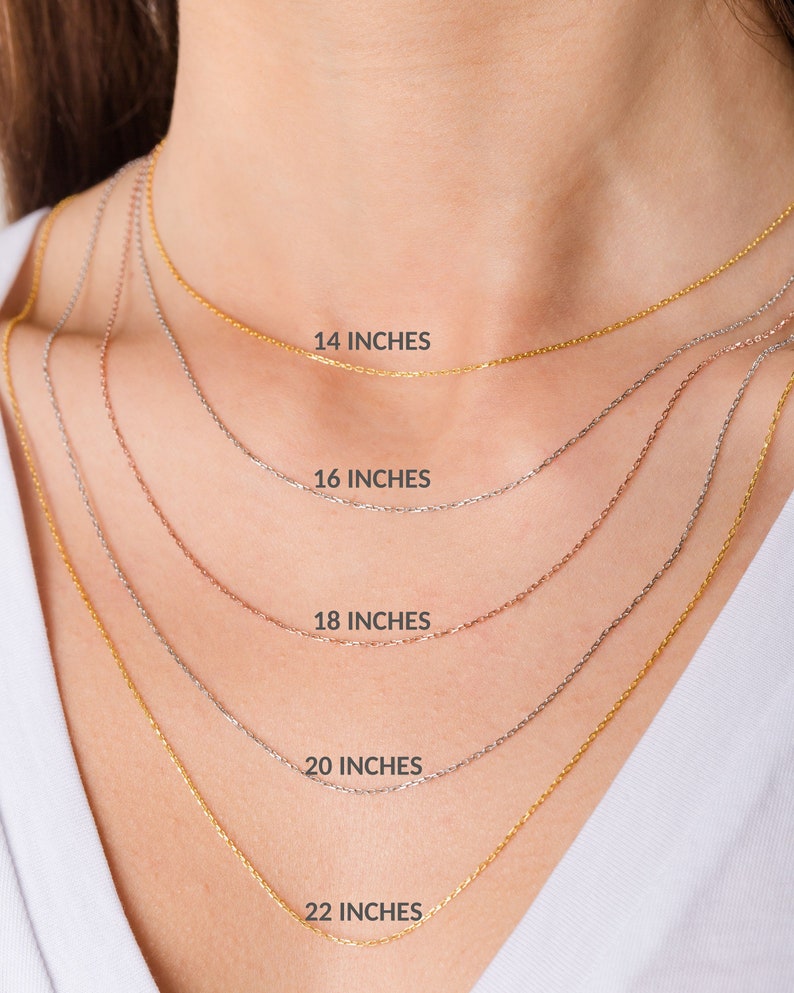 May include: Five gold chains of different lengths, 14 inches, 16 inches, 18 inches, 20 inches, and 22 inches, are shown on a model's neck. The chains are all the same style, with a delicate, cable-link design.