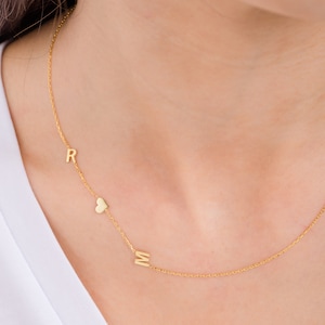 May include: A gold chain necklace with a heart charm and the letters "R" and "M" hanging from it.