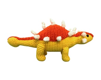 May include: A crocheted stuffed dinosaur toy with a yellow body, orange back, and white spikes.