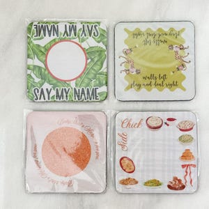May include: Four square coasters with various designs. One features a tropical leaf pattern with the text "SAY MY NAME." Another has a pink and orange speckled design with text. The third has a yellow background with leopard print and text. The last has food illustrations.
