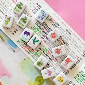 May include: A collection of white tiles with various illustrations and text, including a snake, a bird, and floral designs. The tiles are arranged on a patterned surface with printed text and numbers.