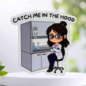 Könnte beinhalten: Ein gestanzter Aufkleber mit einem Cartoon-Wissenschaftler mit dunklem Haar und Brille, der auf einem Hocker vor einem Laborabzug sitzt. Der Text CATCH ME IN THE HOOD ist in Schwarz über der Illustration mit blauen Glasgefäßen gedruckt.
