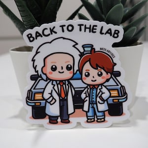 Puede incluir: Una pegatina blanca con una ilustración de dibujos animados de dos personajes con batas de laboratorio blancas de pie frente a una máquina del tiempo DeLorean. El texto "Back to the Lab" está por encima de los personajes y "MedLabVibes" está en la esquina superior derecha.