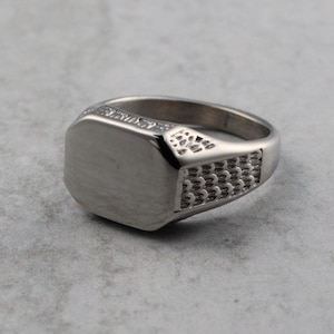 May include: A silver signet ring with a smooth, flat top and a textured band.