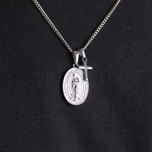 May include: A silver chain necklace with a silver pendant featuring a depiction of the Virgin Mary and a small silver cross.