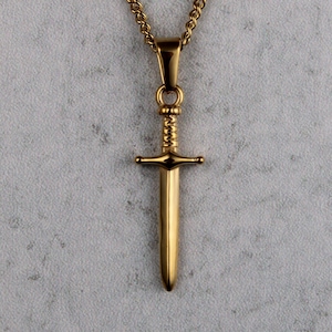 May include: A gold chain necklace with a sword pendant. The sword is detailed with a cross guard and a pointed tip.