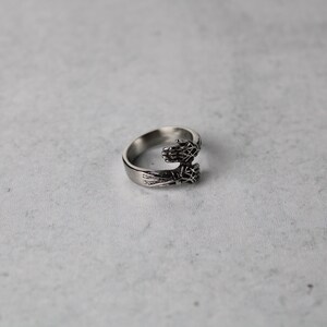 May include: A silver ring with two hands clasped together, forming a circle. The hands are detailed with intricate designs.