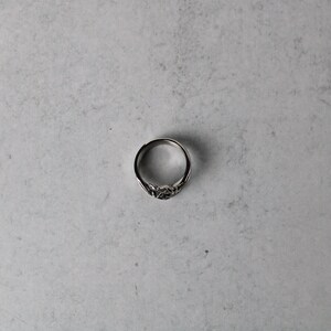 May include: A silver ring with a detailed design. The ring is on a gray background.