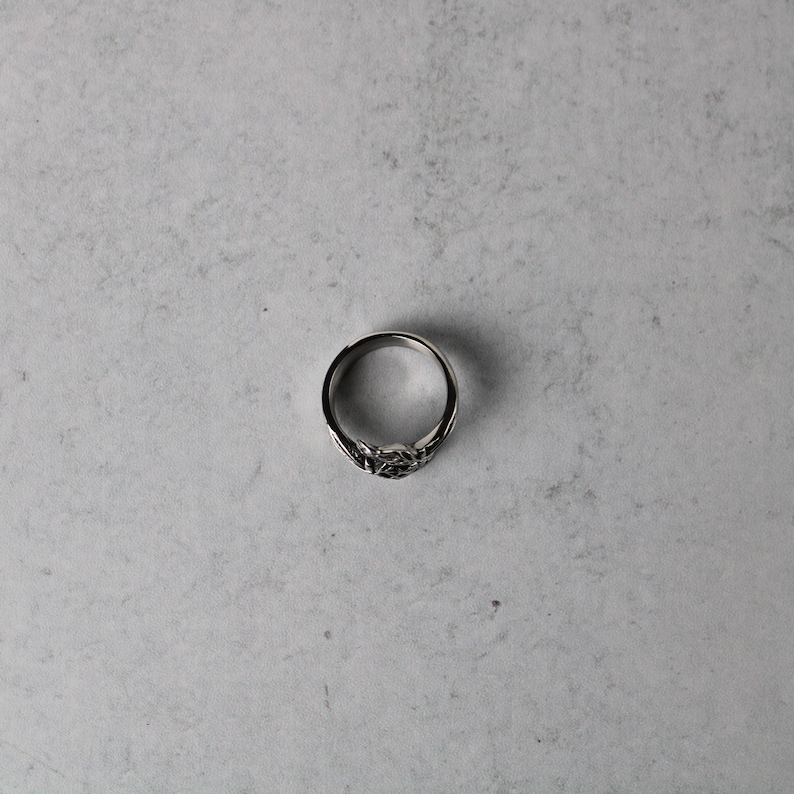 May include: A silver ring with a detailed design. The ring is on a gray background.