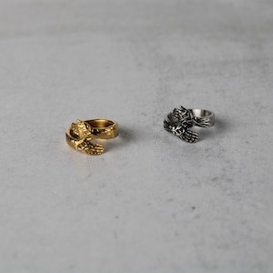 May include: Two rings with a design of two hands clasped together. One ring is gold and the other is silver.