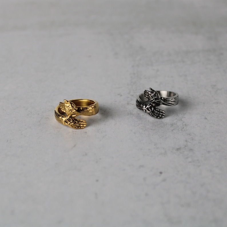 May include: Two rings with a design of two hands clasped together. One ring is gold and the other is silver.