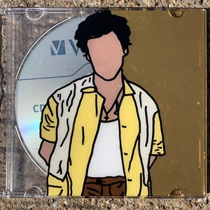 May include: A CD case with a gold background and a black and white illustration of a person wearing a yellow shirt and white undershirt. The person has black hair and a blank face.