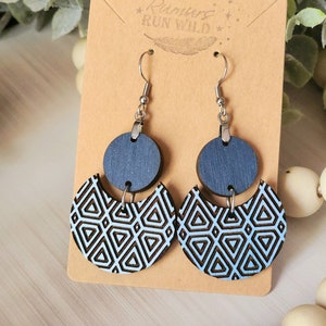 May include: A pair of blue and white geometric patterned wooden earrings with silver hooks. The earrings are displayed on a brown card with the text "Rumors Run Wild" printed on it.