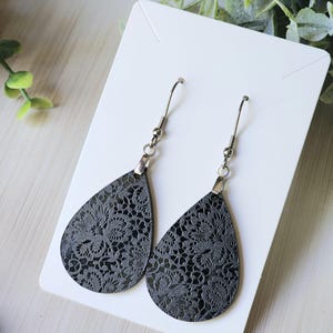 May include: A pair of black teardrop-shaped earrings with a delicate lace pattern. The earrings have silver hooks.