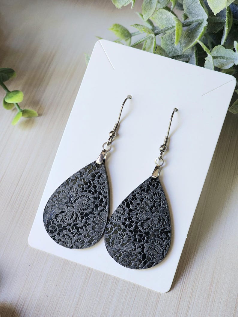 May include: A pair of black teardrop-shaped earrings with a delicate lace pattern. The earrings have silver hooks.