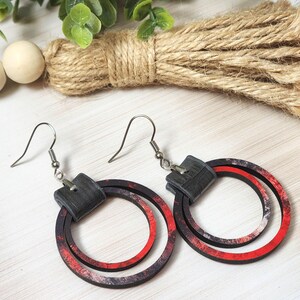 Puede incluir: Un par de pendientes de aro con un dise&ntilde;o en capas. Los pendientes presentan una parte superior cuadrada negra y dos c&iacute;rculos conc&eacute;ntricos rojos y negros. Los pendientes son de madera y tienen ganchos plateados.