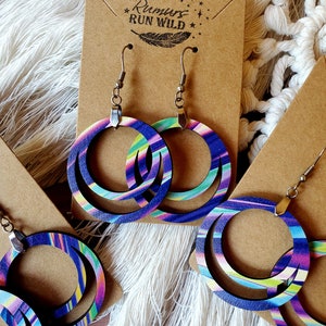 May include: A pair of wooden hoop earrings with a multi-colored swirl pattern. The earrings are on a brown card with the text "Rumours Run Wild" and a feather design.