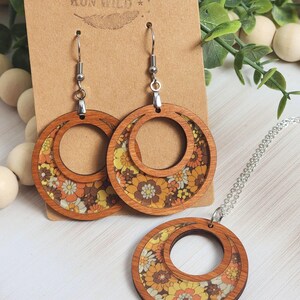 May include: Wooden earrings and necklace set with a floral pattern in shades of orange, yellow, and white. The earrings are hoop-shaped, and the necklace has a matching pendant. The brand name "Rumors Run Wild" is printed on the backing card.