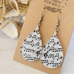 May include: A pair of silver teardrop earrings with a music sheet design. The earrings are on a brown card with the text "Rumours Run Wild" printed on it.