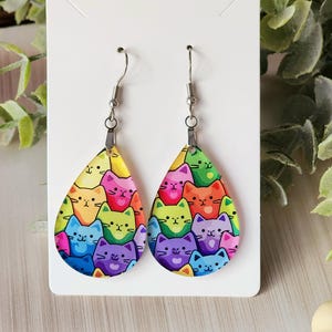 May include: A pair of teardrop-shaped earrings with a rainbow cat print. The earrings are made of clear resin and have silver hooks.