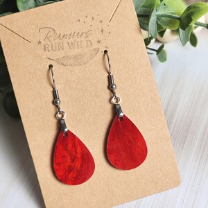 May include: A pair of red teardrop earrings with silver-colored hooks. The earrings are displayed on a brown card with the text "Rumors Run Wild" and a feather graphic.