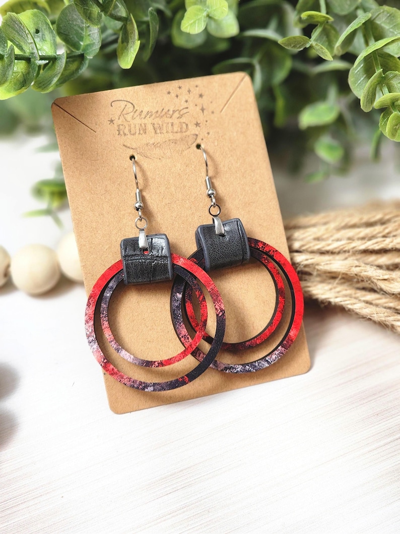 Puede incluir: Pendientes de aro con un dise&ntilde;o en capas. Los pendientes presentan un patr&oacute;n veteado rojo, negro y blanco en los aros, con un cuadrado negro similar al cuero en la parte superior. Los pendientes se exhiben en una tarjeta marr&oacute;n con el texto "Rumors Run Wild".
