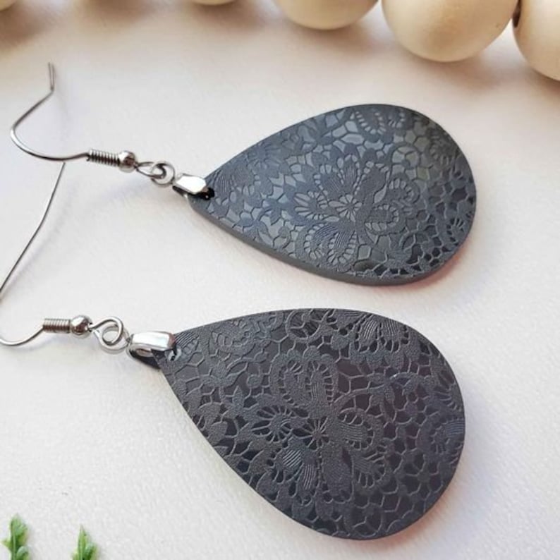 May include: A pair of teardrop-shaped earrings with a black lace pattern. The earrings have silver hooks.