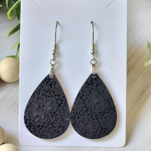 May include: A pair of black teardrop-shaped earrings with a delicate lace pattern. The earrings have silver hooks.