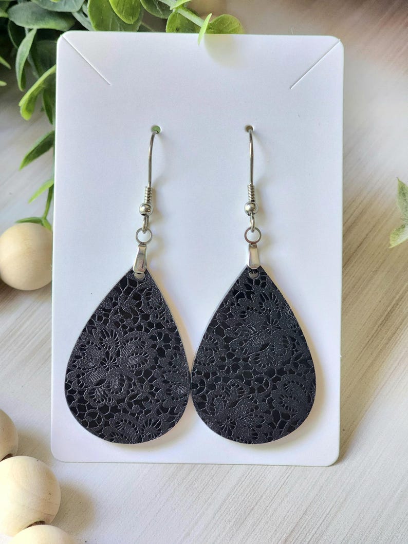 May include: A pair of black teardrop-shaped earrings with a delicate lace pattern. The earrings have silver hooks.