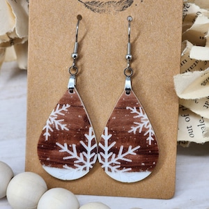 May include: A pair of dangle earrings with a brown and white snowflake design. The earrings are made of metal and have a teardrop shape.