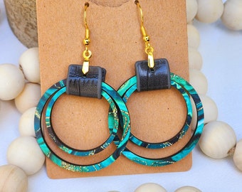 May include: A pair of green and gold double hoop earrings with black leather accents. The earrings are on a brown card with the text "Run Wild" in gold lettering.