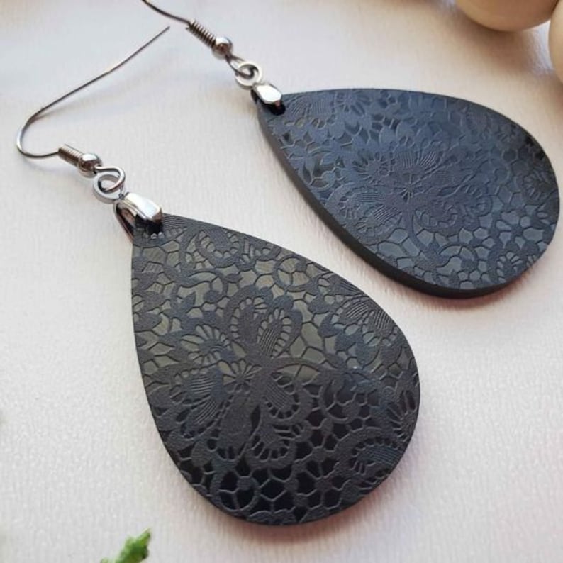 May include: A pair of black teardrop-shaped earrings with a delicate lace pattern. The earrings have silver hooks.