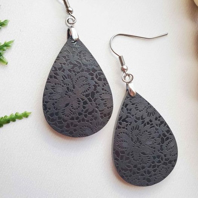 May include: A pair of black teardrop-shaped earrings with a delicate lace pattern. The earrings are made of metal and have a hook closure.